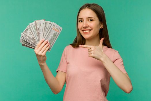 Portrait of a cheerful young woman holding money banknotes and celebrating isolated on blue background