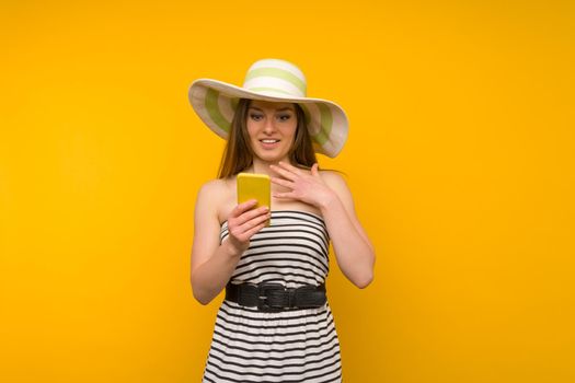 Girl wears straw hat and short white strips dress with open shoulders surprised by the news on a smartphone - image