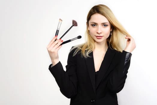 Attractive blonde Make-up artist holding brushes on white background