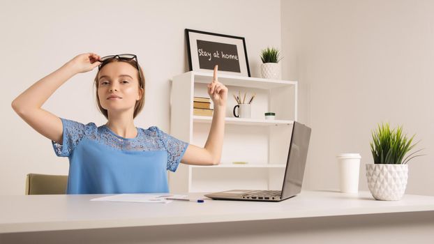 Cute girl in the office shows a finger to the inscription stay at home. - image