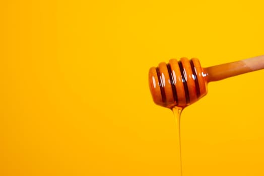 Dripping honey from spoon against yellow background.