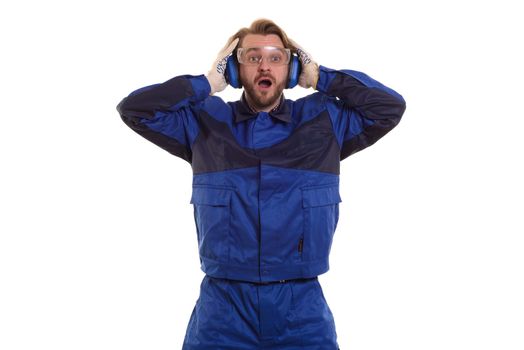 Surprised worker in safety glasses is standing with his mouth holding his headphones.