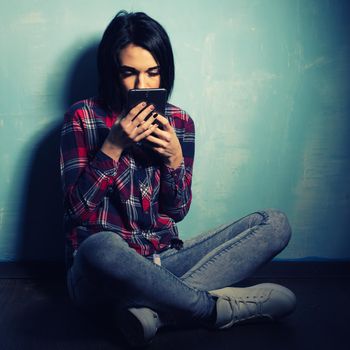 Young sad girl suffering from dependence on social networks sitting on the floor with a smartphone Toned