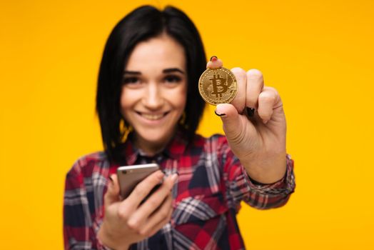 Blurred smiling woman holding a Bitcoin in her hand and showing it - Image