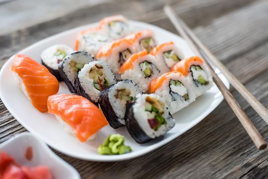 various Japanese sushi on white plate with chopsticks on wooden background