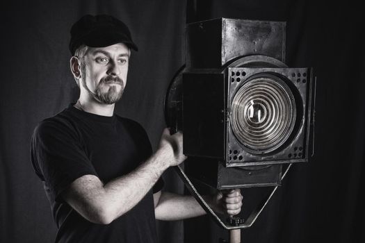 Man wearing a cap stands near a stage spotlight on black background. black and white