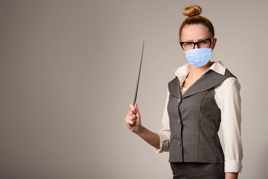 Portrait of young teacher in mask holding pointer. Slim girl in a suit near the wall. Coronavirus Outbreak Defense Concept