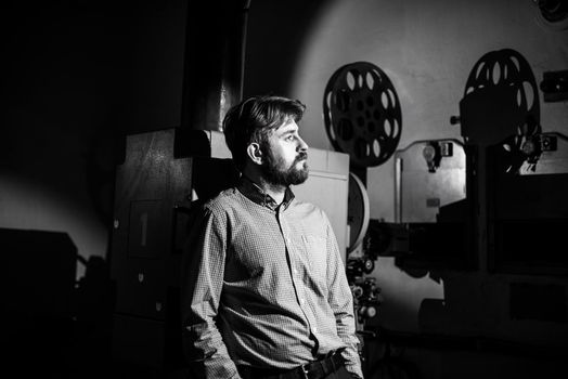 beautiful hipster man standing near a film projector in the room projectionist