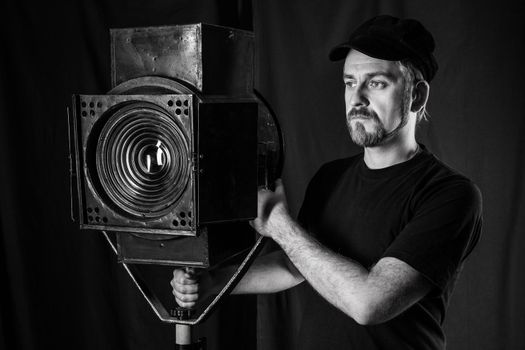 Man wearing a cap stands near a stage spotlight on black background. black and white