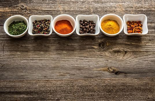 aromatic spices in bowls in horizontal row on wooden background
