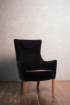 Luxurious black velor armchair stands near the textural wall on a dark wooden floor.