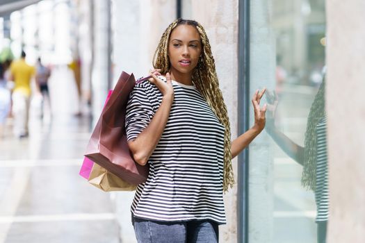 Young black woman in front of a shop window in a shopping street. Female with african braids.