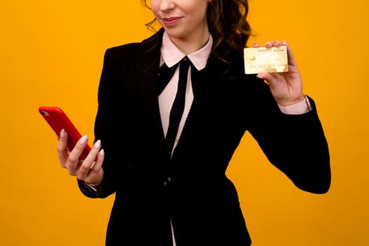 Photo of pleased young woman posing isolated over yellow wall background using mobile phone holding debit card. - image