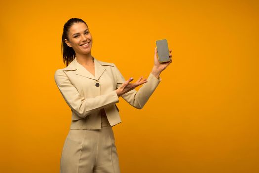 Young girl with facial skin problems posing with a smartphone on a yellow background.