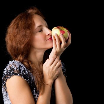 Joyful woman holding fresh apple. Portrait of girl smiling at camera against black background. Happy woman with brown hair posing with ripe healthy fruit in studio