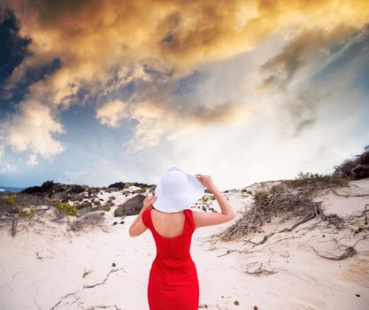 beautiful young woman in evening red dress and white hat in sunset