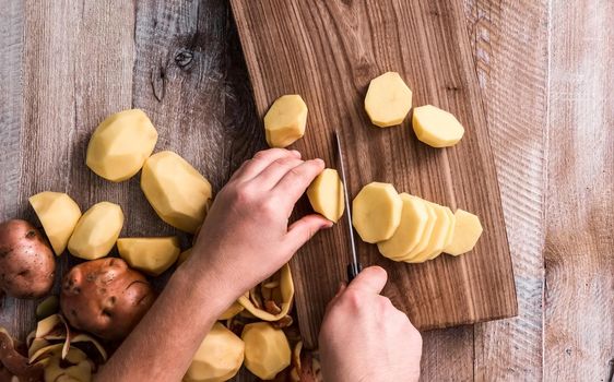 hands cutting potato on wooden board