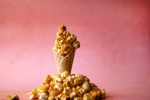 Popcorn spill out from waffle ice cream cone on pastel colorful background. Blue and caramel Popcorn on a cone cornucopia Top view bright hipster background.