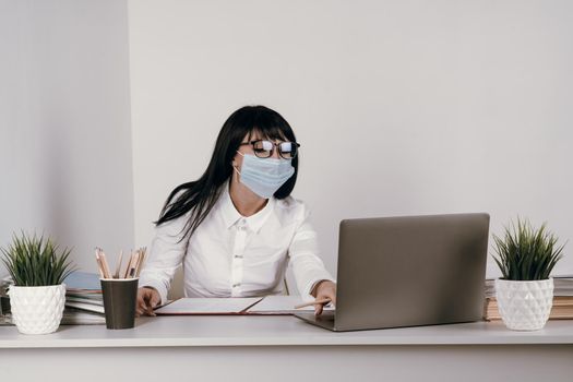 A young woman works remotely in the office with a protective mask during an epidemic.