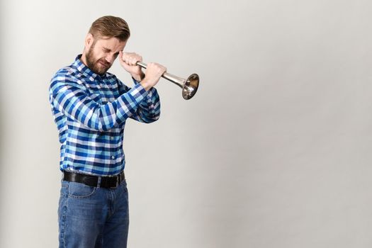 Bearded man in a plaid shirt looks at the horn isolated on grey background