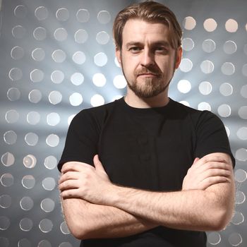 Portrait of man in a black T-shirt standing on stage in the smoke with his arms crossed