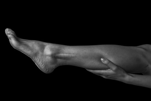 Woman holds her leg, pain in the female calf muscle, monochrome image