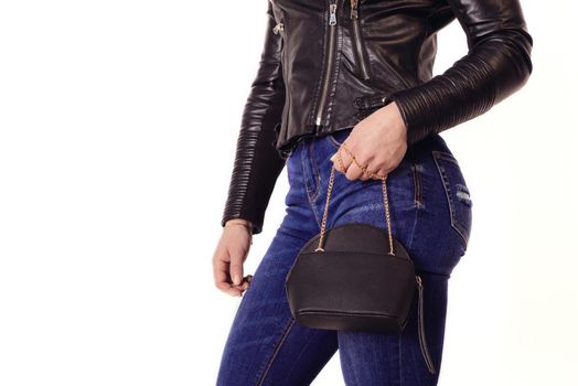 athletic girl in leather jacket and jeans holds purse on chain isolated on white background
