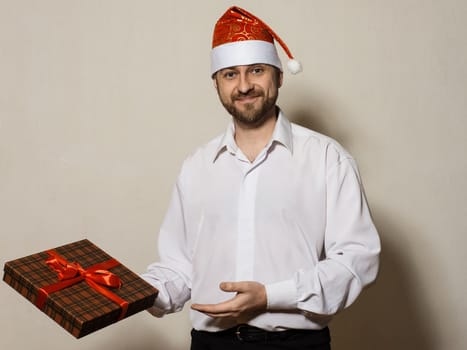 Handsome man in white shirt and Christmas cap holding gift box tied with a red ribbon