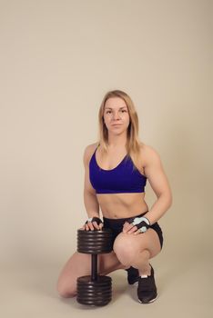 athletic woman bodybuilder sits with a heavy dumbbell on a gray background