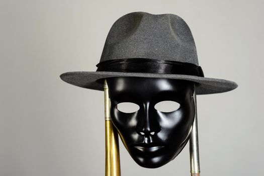 Black theater mask and hat hanging on a brass pipe on gray background with copy space. Social masking and mystery concept