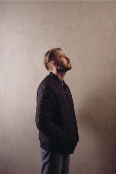 An attractive middle-aged bearded man in a black jacket and jeans stands behind the wall looking sideways to the top. copy space. deadpan without retouching