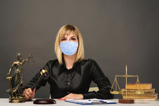 A young fair woman judge in protective mask works in her office. - image