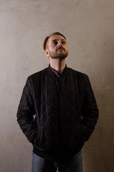 An attractive middle-aged bearded man in a black jacket and jeans stands behind the wall llooks up. copy space. deadpan without retouching