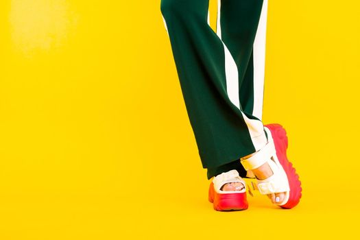 Women's legs in sport sandals with red soles and green pants with stripes on a yellow background.
