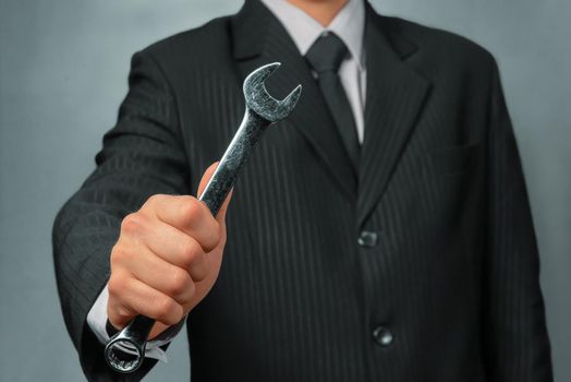 Businessman in a suit holds spanner, focus on spanner, concept of business creation
