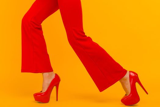 The business woman running somewhere hurrying up isolated on yelow background. Stylish red heels and pants on thin female legs
