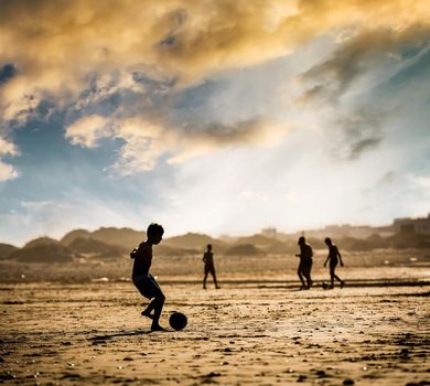 Silhouette of the boy on the beach with a ball at sunset