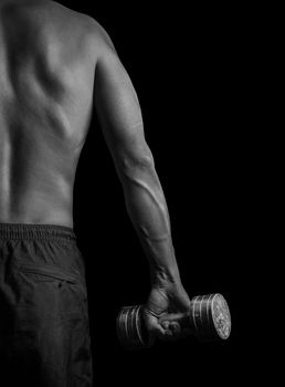 Unrecognizable muscular man exercises with dumbbell, rear view, monochrome image