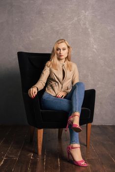 Adalt lady in jeans and a leather jacket posing in the armchair having a rest