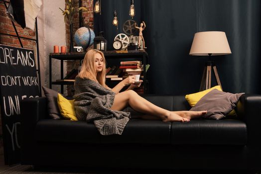 A woman sitting on the couch with a cup in her hands and smiling as she looks in front of her.