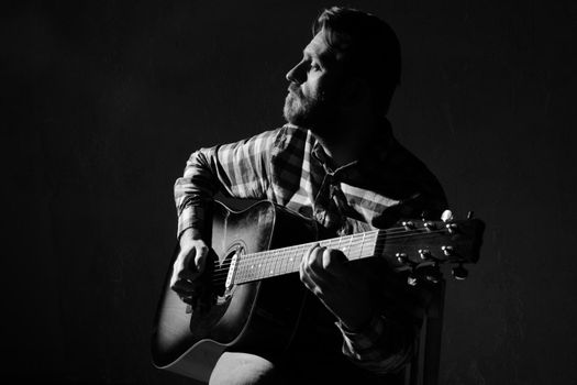 Sad Caucasian male musician playing guitar on stage, focus on hand. black and white.