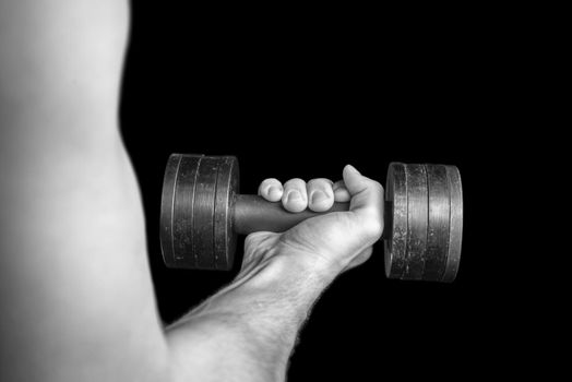 Male muscular hand holds a dumbbell, monochrome image