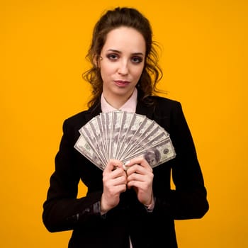 Woman showing a stack of money with her finger isolated on yellow background.