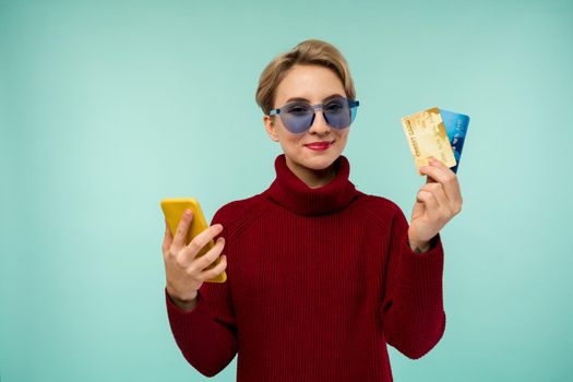 Photo of pleased young woman with acne problem face skin posing isolated over blue wall background using mobile phone holding debit card. - image