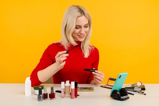 Candid shot of cute young Caucasian woman blogger presenting beauty products and broadcasting live video to social network, using brush to apply mascara while recording everyday make up tutorial