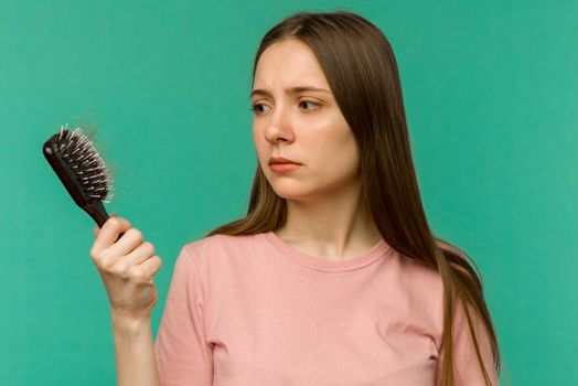 Young girl with a comb and problem hair on blue background - image