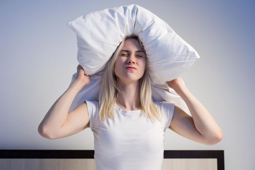 Young woman covering ears with pillow because of noise. - image