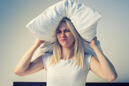 Young woman covering ears with pillow because of noise. - image toned