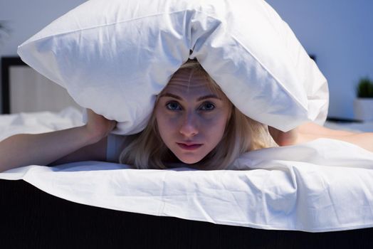 Female lying on bed and closing her ears with pillow - image