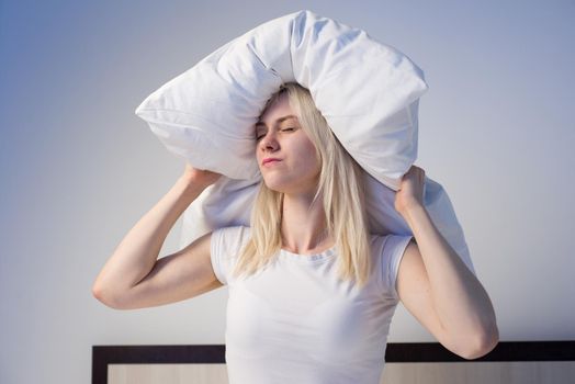 Young woman covering ears with pillow because of noise. - image